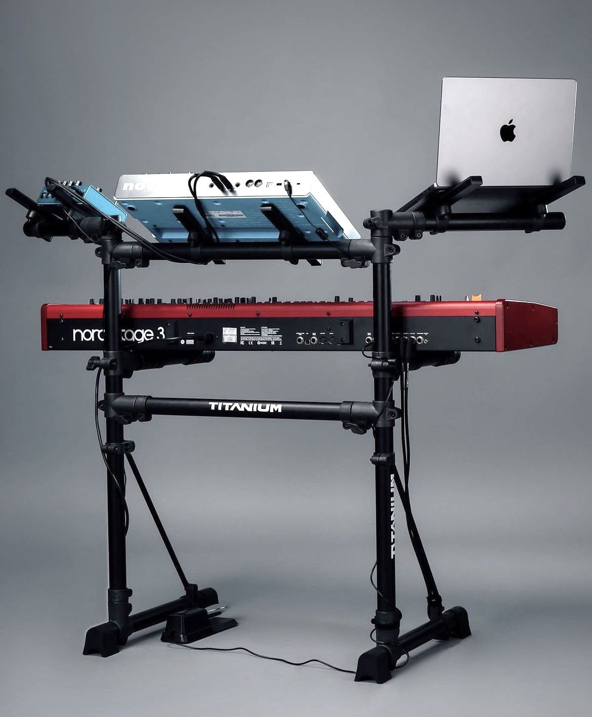 A double-tier keyboard stand holding a Nord Stage 3 on the lower tier and a synth and laptop up top